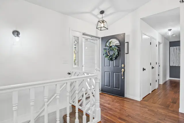 This entryway features a dark front door with a wreath, white railings, and hardwood floors.