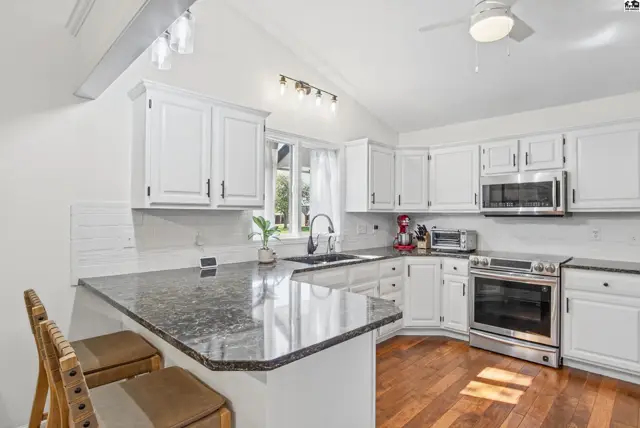 This kitchen features white cabinets, granite countertops, stainless steel appliances, and a vaulted ceiling.