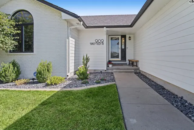 A concrete walkway leads to a white-brick home with a covered entryway and landscaping.