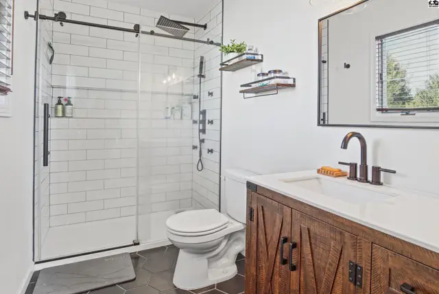 Modern bathroom features a walk-in shower, wood vanity, and dark hexagonal floor tiles.