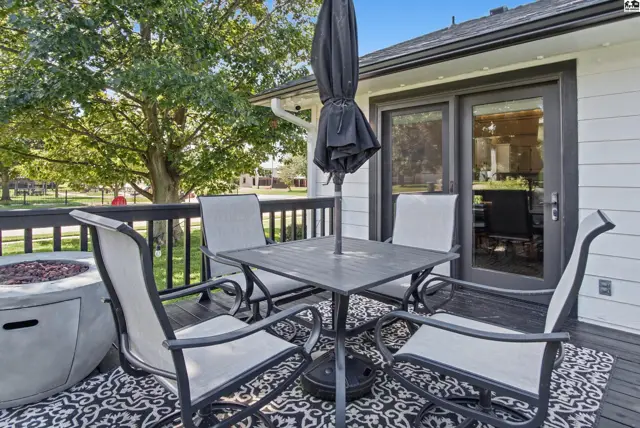 Deck with seating, umbrella, fire pit, and outdoor rug adjacent to a white-sided home.
