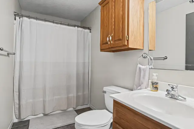 This bathroom features a white toilet, vanity with wood cabinets, and a shower with a white curtain.