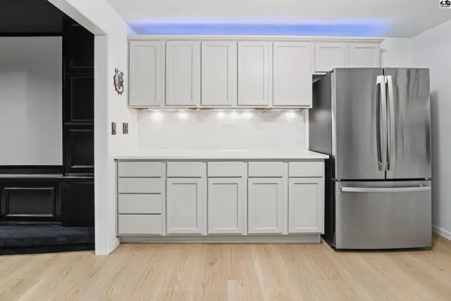 Light grey cabinets and white countertops complement a stainless steel refrigerator.