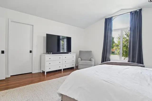 Spacious bedroom with hardwood floors, a large window, and a white dresser.