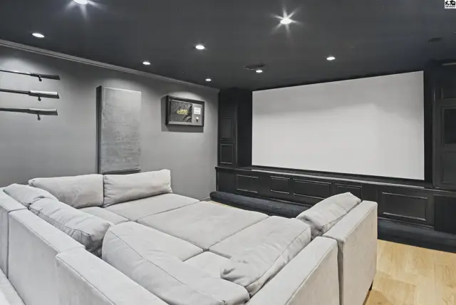 Spacious room with a large projection screen, sectional sofa, and wood flooring.