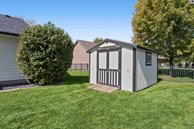 White storage shed with double doors and a small window sits on a green lawn.