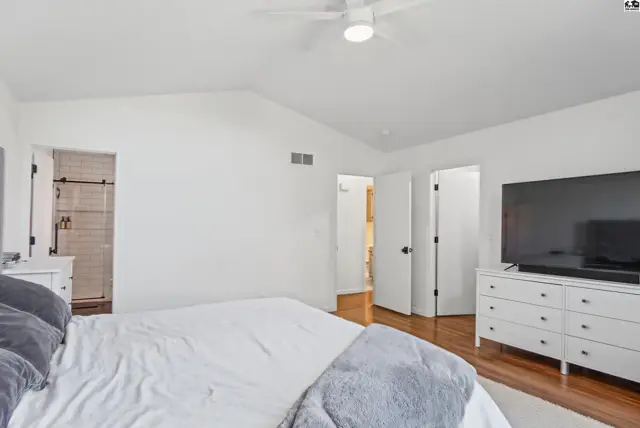 Spacious bedroom with vaulted ceiling, ceiling fan, and access to a bathroom.
