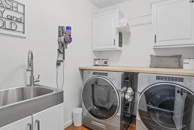 This laundry room features a stainless steel sink, white cabinetry, and a stacked washer and dryer.
