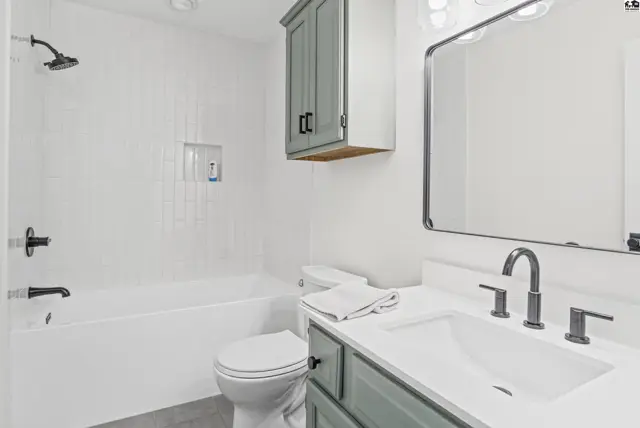 This bathroom features a white tub, toilet, vanity with a sink, and a large mirror.