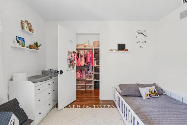 White dresser, changing pad, and a bed with grey bedding are in a room with a walk-in closet.