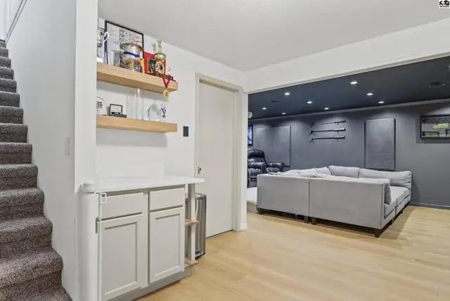 Carpeted stairs lead to a finished basement with a gray sectional and wood-look flooring.