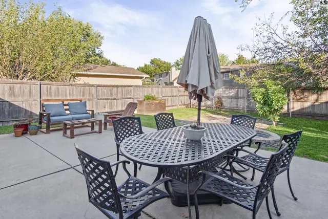 Paved patio with outdoor dining set and seating area surrounded by a wooden fence.