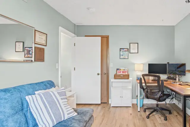 A room features a blue sofa, a desk with computers, and a large mirror.