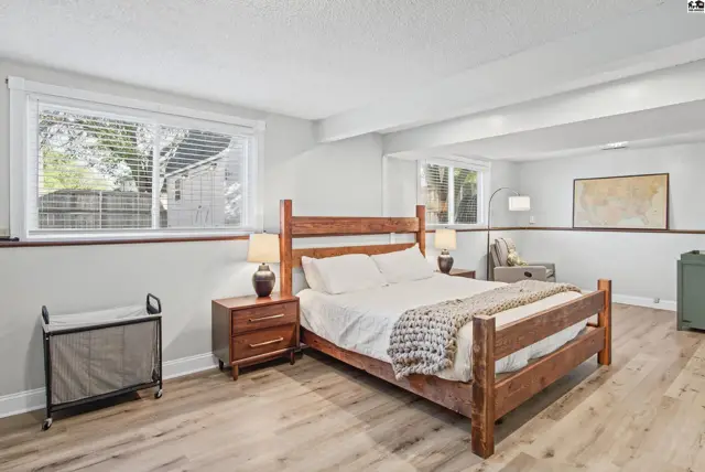 Spacious bedroom features a wooden bed frame, two nightstands, and light wood flooring.
