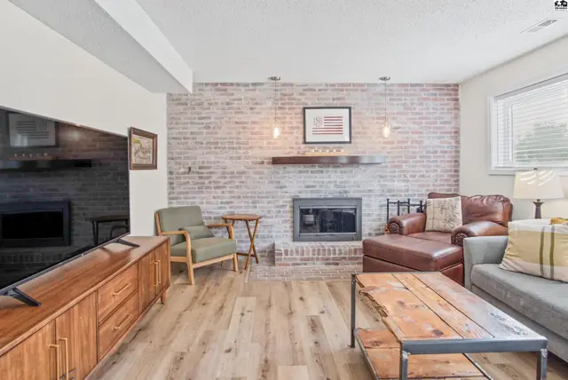 Living room features a brick fireplace, wood floors, and a large entertainment console.