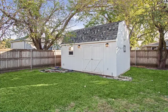 White shed with double doors and two exterior lights sits in a fenced yard.