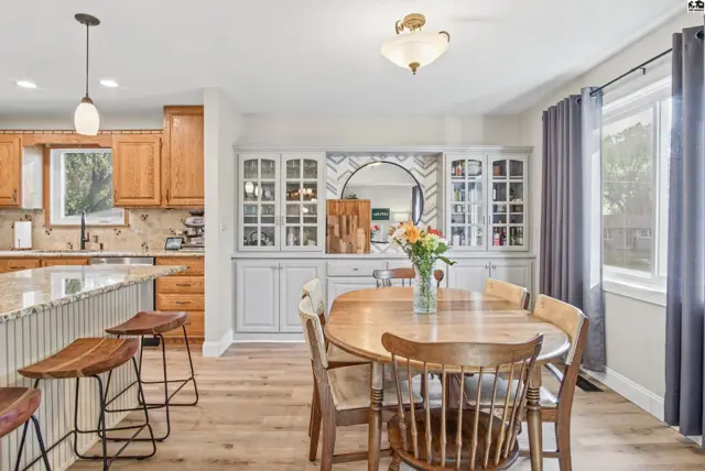 A dining area with a wooden table and chairs is adjacent to a kitchen with granite countertops.