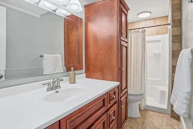 This bathroom features a white vanity, a large mirror, and a tiled shower stall.