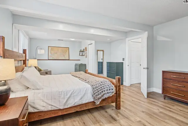 Spacious bedroom with light blue walls, wood floors, and a raised sitting area.