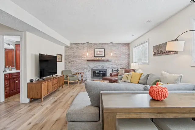 Spacious living area with a brick fireplace, wood-look flooring, and a modern entertainment console.