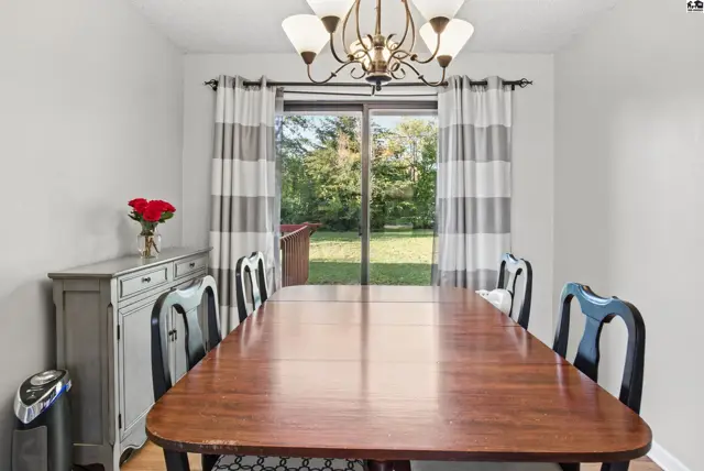 A wood dining table with chairs sits before a sliding glass door with striped curtains.