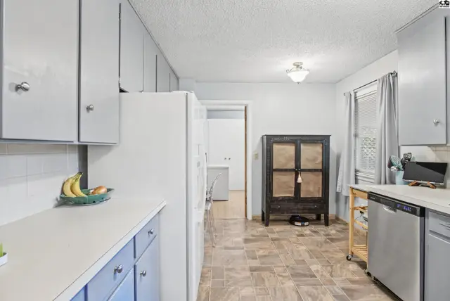 This kitchen features white cabinets, a white refrigerator, and a dishwasher.