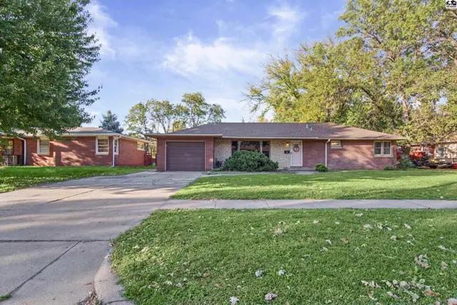 Brick ranch home with attached garage and mature trees on a grassy lot.