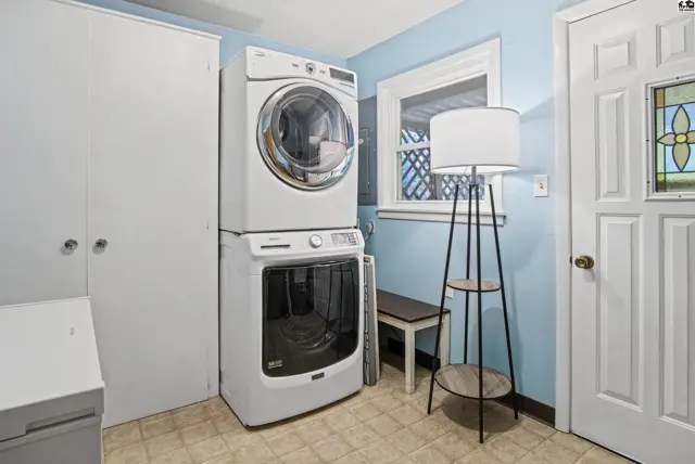 This laundry room features a stacked washer and dryer, a white storage cabinet, and a door with stained glass.