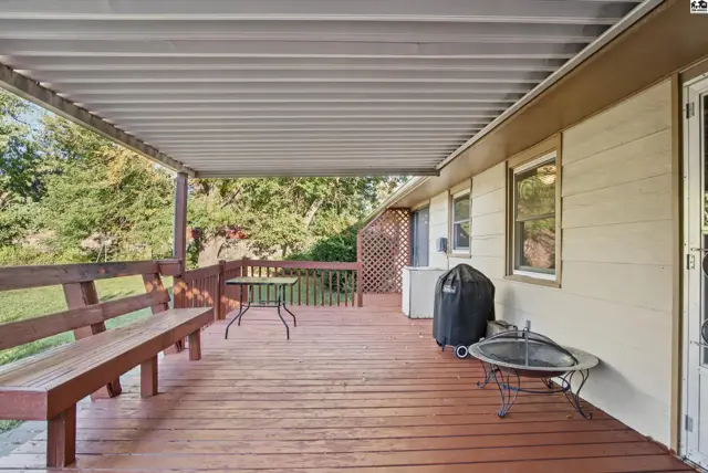Covered wooden deck with built-in bench, table, grill, and fire pit.