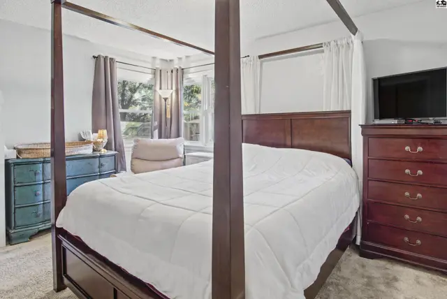 Spacious bedroom features a four-poster bed, dresser, and large window.