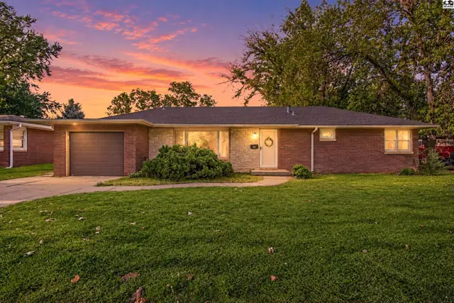 Brick ranch home with attached garage, manicured lawn, and mature trees.