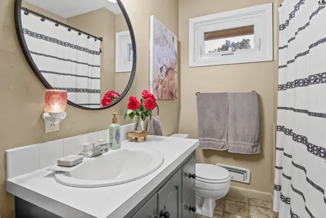 This bathroom features a white vanity with a sink, a round mirror, and a toilet.