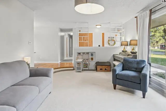 Spacious living room with carpet, a piano, and large windows overlooking the yard.