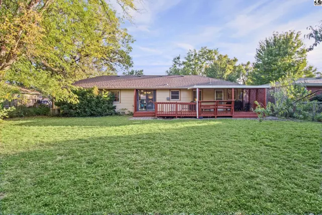 A single-story home features a covered patio and a wooden deck overlooking a grassy yard.