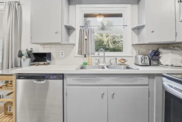 Light gray cabinets and countertops frame a double sink and window above the dishwasher.