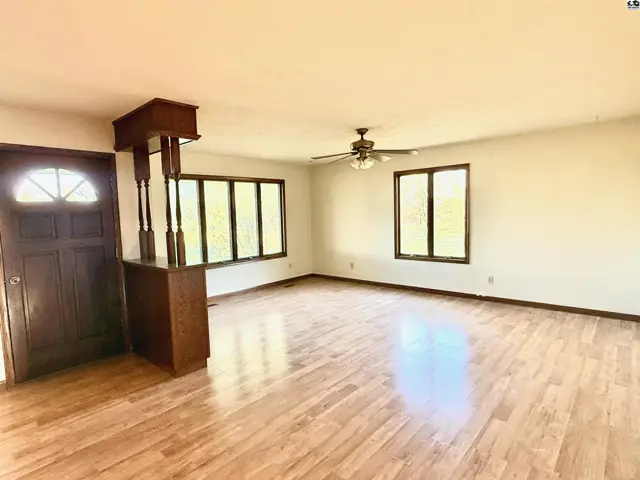 Spacious living area with wood-look flooring, a ceiling fan, and large windows.