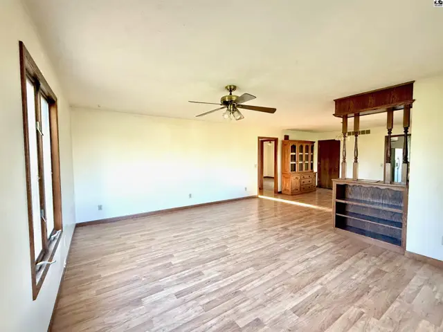 Spacious living area with wood-look flooring, a ceiling fan, and a built-in bar.