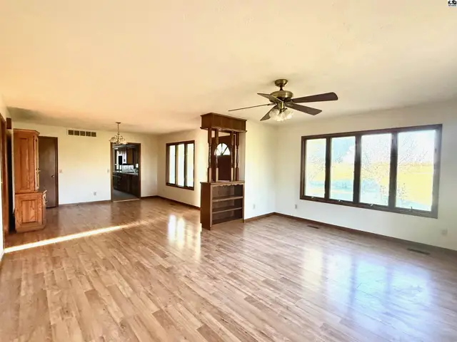 Spacious living area with hardwood floors, large windows, and a ceiling fan.