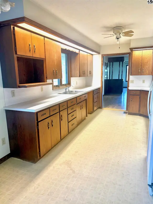 This kitchen features ample wooden cabinetry, white countertops, and a ceiling fan.