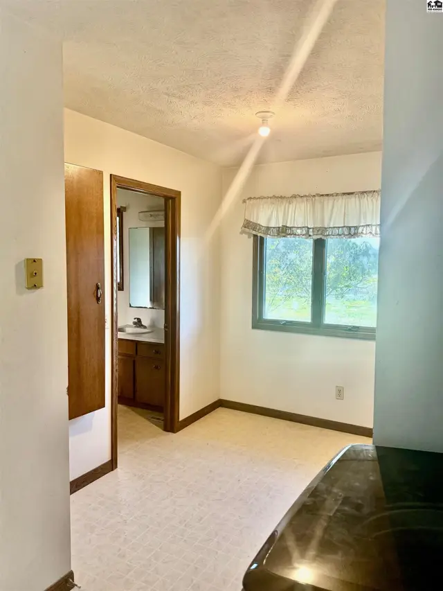 This room features a window with a valance, wood cabinetry, and a doorway to a bathroom.