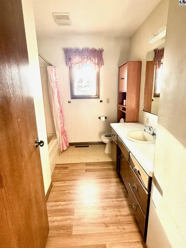 This bathroom features a bathtub, vanity with sink, toilet, and wood-tone cabinetry.