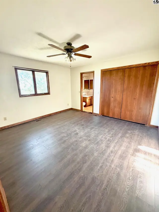 Spacious room with dark wood flooring, a ceiling fan, and a large closet.