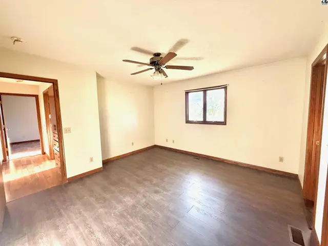 Spacious room with dark wood flooring, a ceiling fan, and a window.