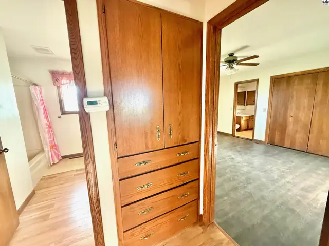 Wood cabinetry with brass hardware stands beside a doorway to a room with a ceiling fan.