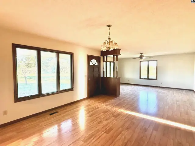 Spacious living area with hardwood floors, large windows, and a chandelier.