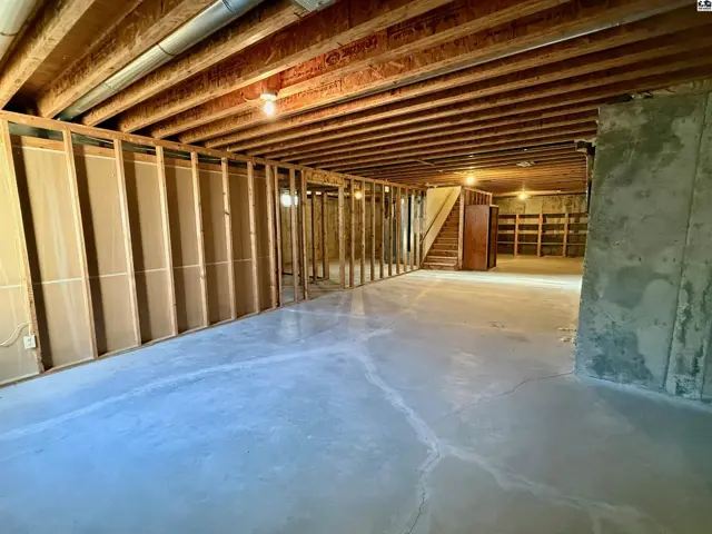 Unfinished basement with concrete floor, exposed wooden beams, and framed walls.