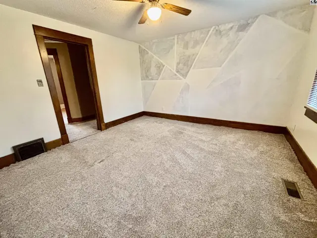 Carpeted room with a ceiling fan and a geometric accent wall.