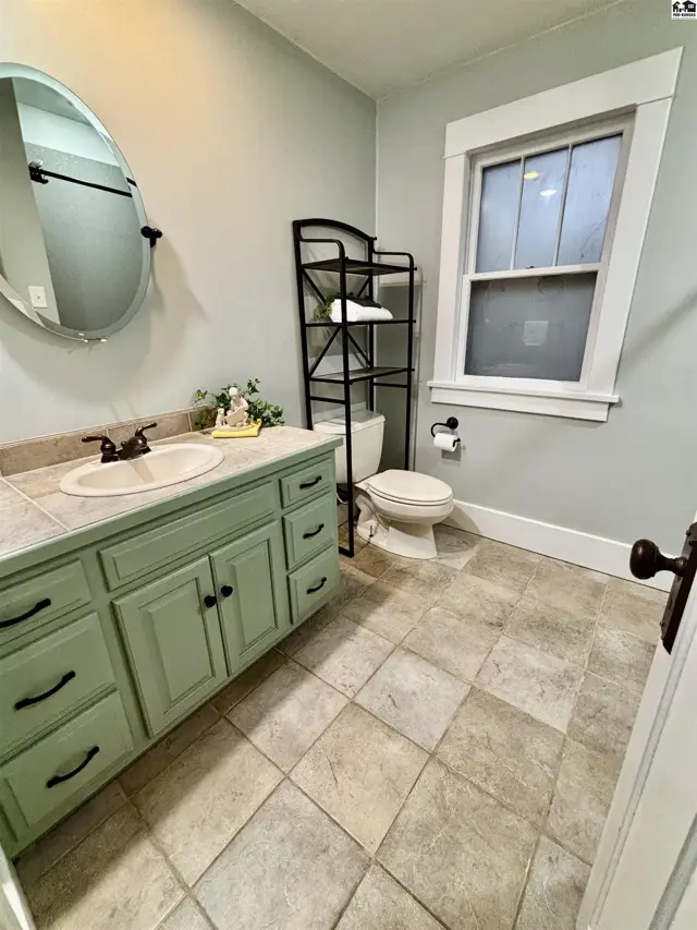 This bathroom features a light green vanity, tiled floor, and a large oval mirror.