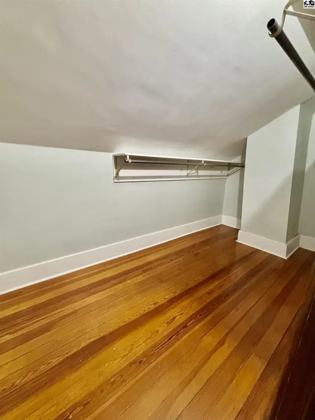 This room features hardwood floors, white baseboards, and a built-in closet rod.