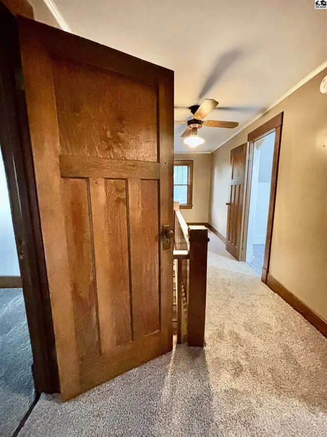 Hallway with plush carpet, wooden doors, and a ceiling fan.